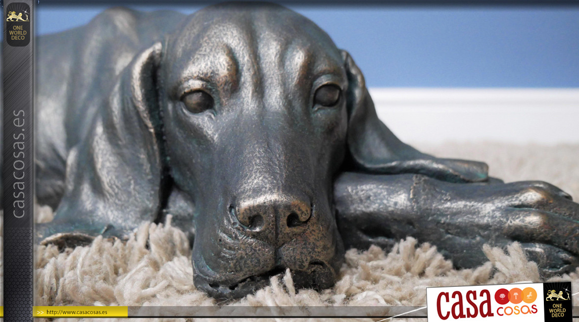 Representación de un perro acostado en resina con acabado negro carbón y reflejos bronce, ambiente campestre, 58cm.