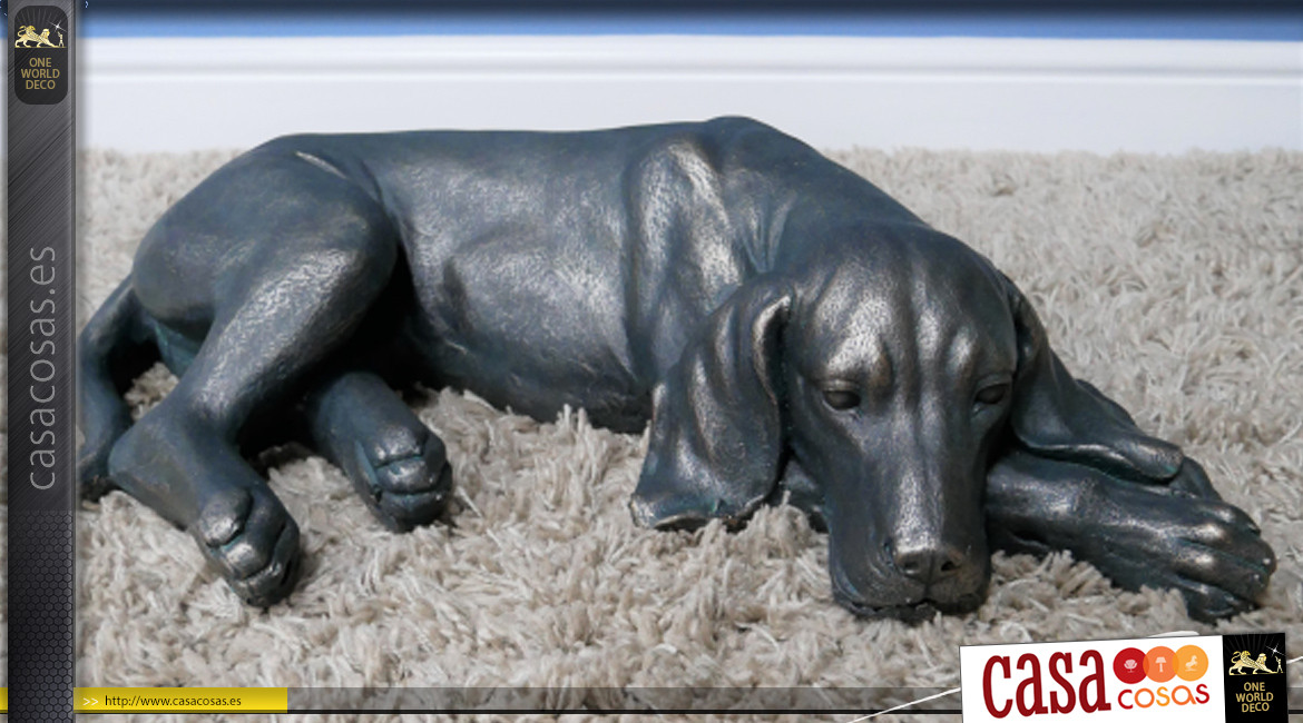 Representación de un perro acostado en resina con acabado negro carbón y reflejos bronce, ambiente campestre, 58cm.